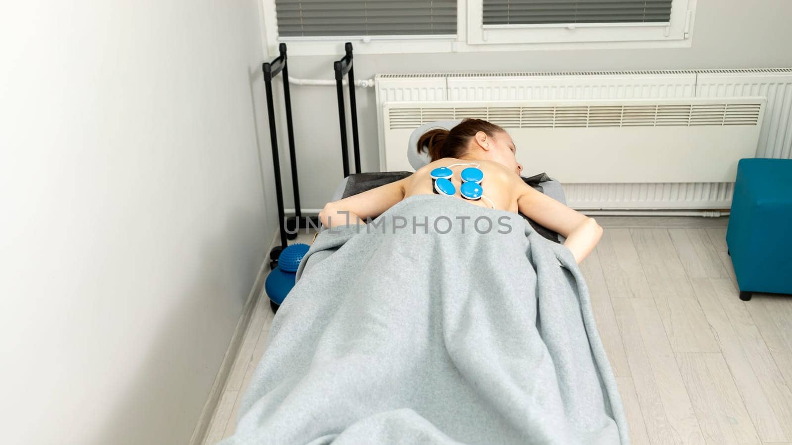 Young Woman With Cerebral Palsy, Scoliosis Lying on Couch Under Wireless Electric Muscle Stimulator, Getting Massage. Pain Treatment of Woman's Back. Rehabilitation,Medical Equipment.Horizontal plane.