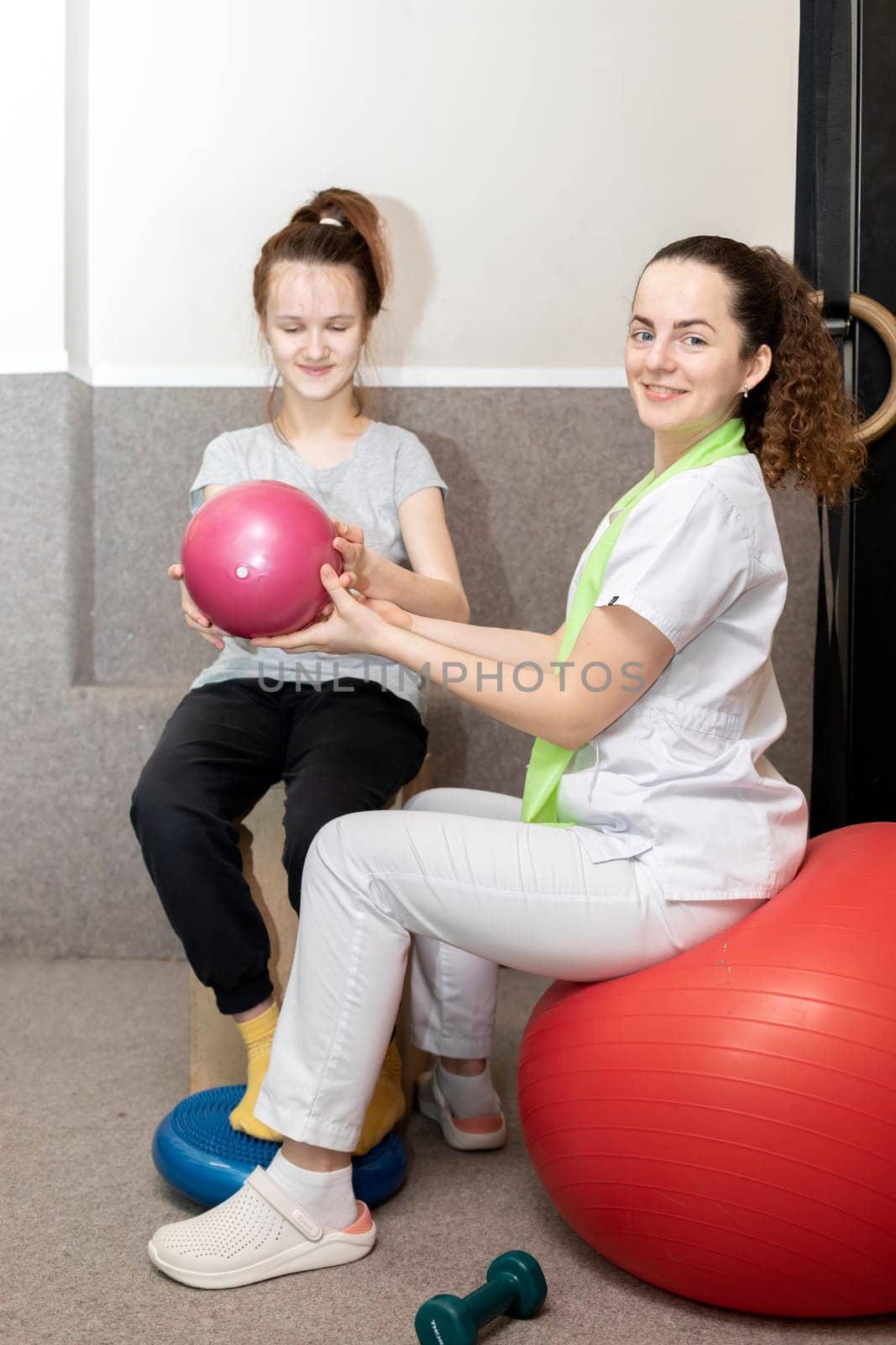 Smiling Child, Teenage Girl With Disability Does Physical Exercises With Support Of Rehabilitation Specialist, Physical Therapist. Rehabilitation. Musculoskeletal Disorder. Vertical plane.