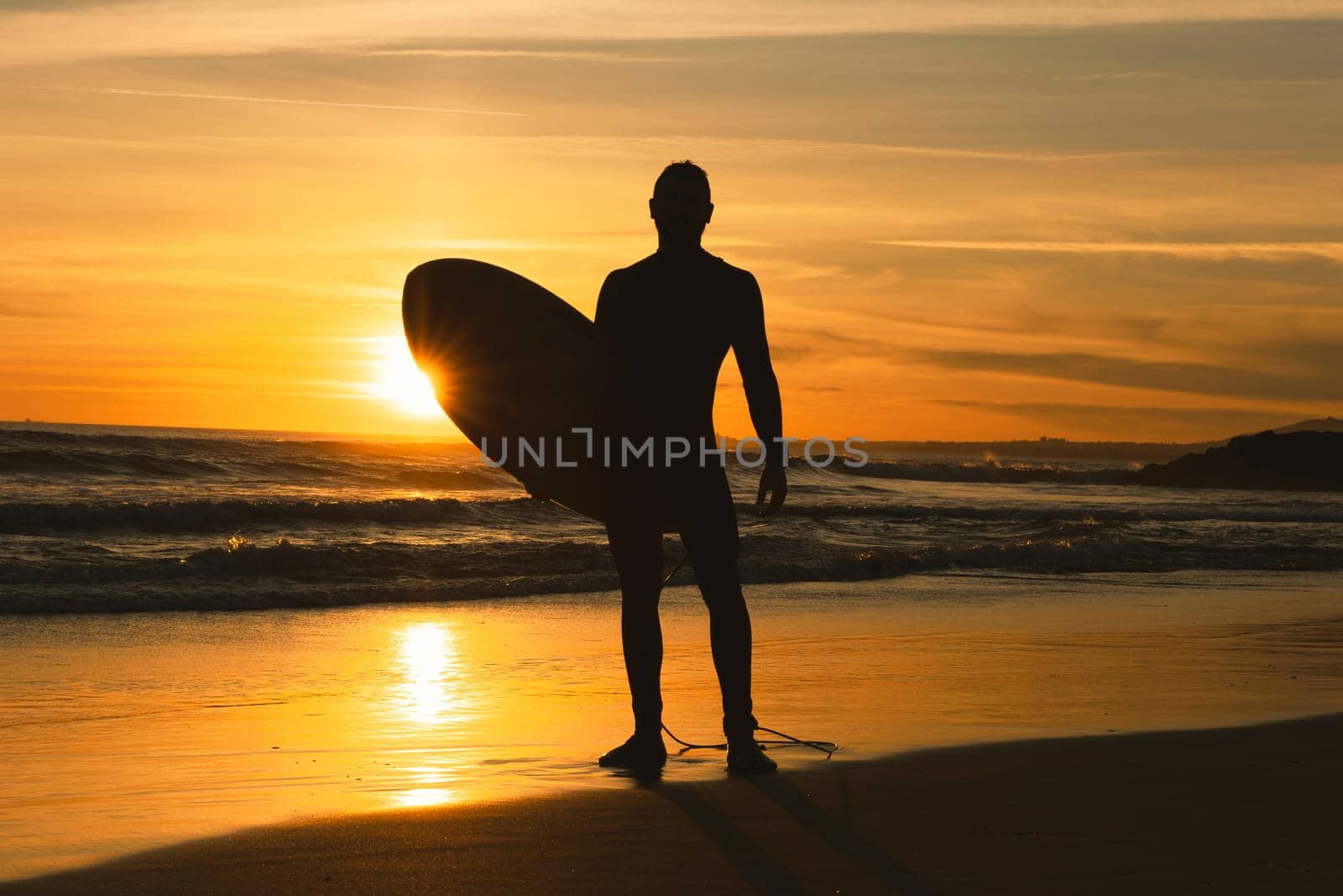 Silhouette of a man surfer holding surfboard on the seashore. Mid shot