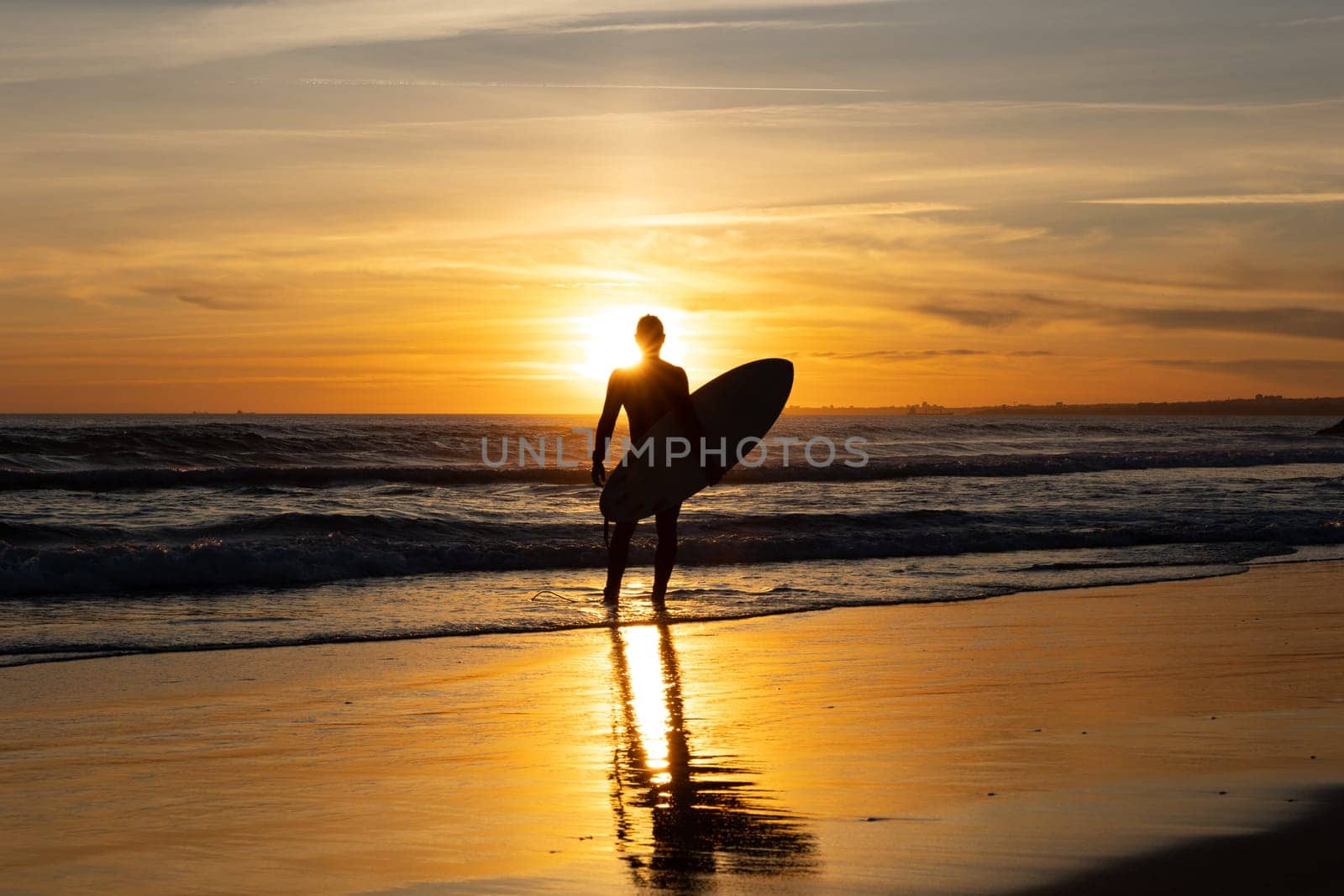 Silhouette of a man surfer holding surfboard standing alone on the seashore. Mid shot
