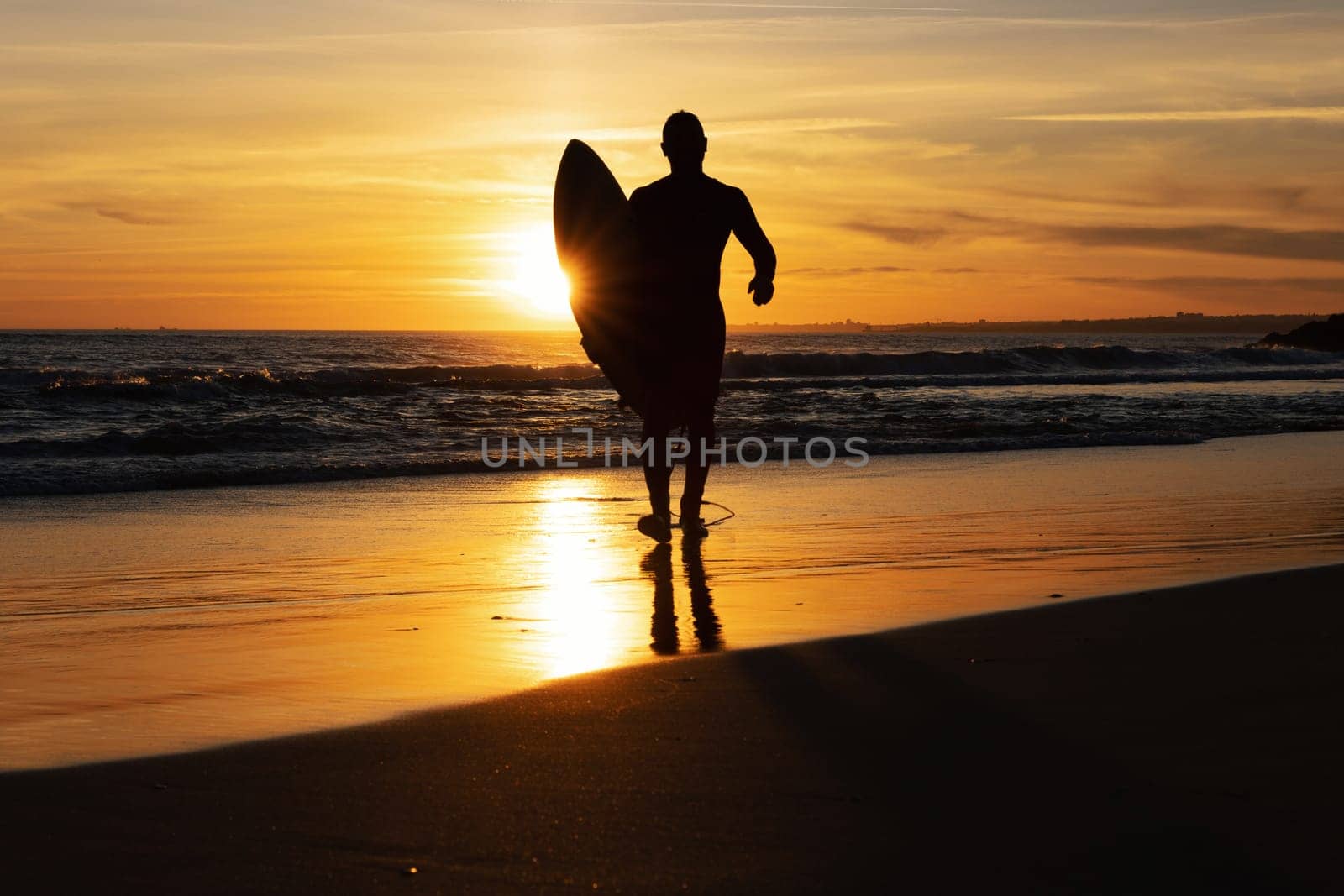 Silhouette of a man surfer walking out on the seashore at sunset. Mid shot