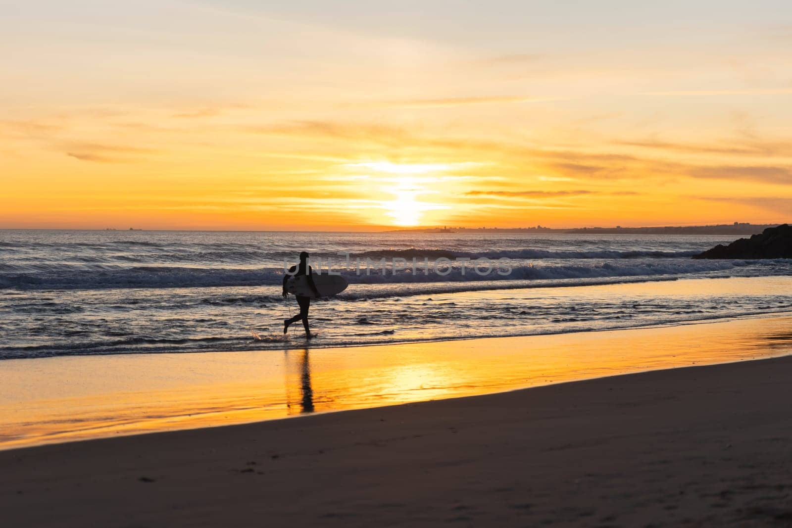 A man surfer running on the seashore at bright orange sunset. Mid shot