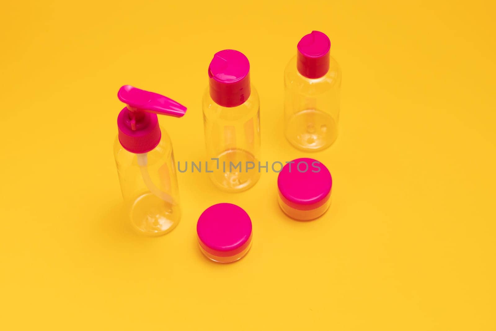 Cosmetic plastic clear fuchsia travel bottle kit for soap, cream, shampoo, gel, lotion, liquids. Toiletries Beauty Kit on yellow orange background. Airplane approved luggage container size. Copy space