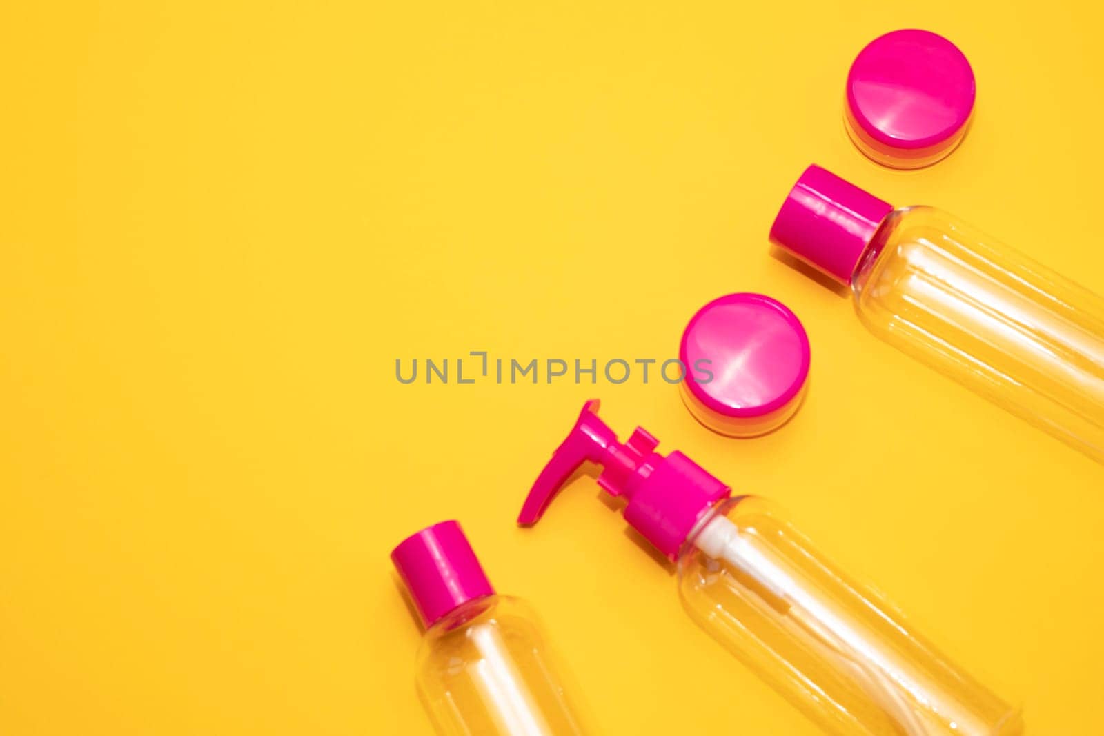 Flatly fuchsia travel bottle kit for liquids, cream. Toiletries Beauty Kit on yellow orange background. Airplane approved luggage reusable container size. Summer time, vacation. Horizontal. Copy space