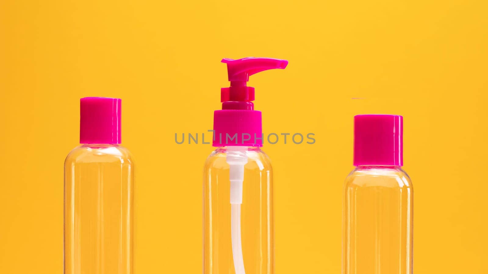 Closeup fuchsia travel bottle kit for liquids, cream. Toiletries Beauty Kit on yellow orange background. Airplane approved luggage reusable container size. Summer time, vacation concept. Horizontal.