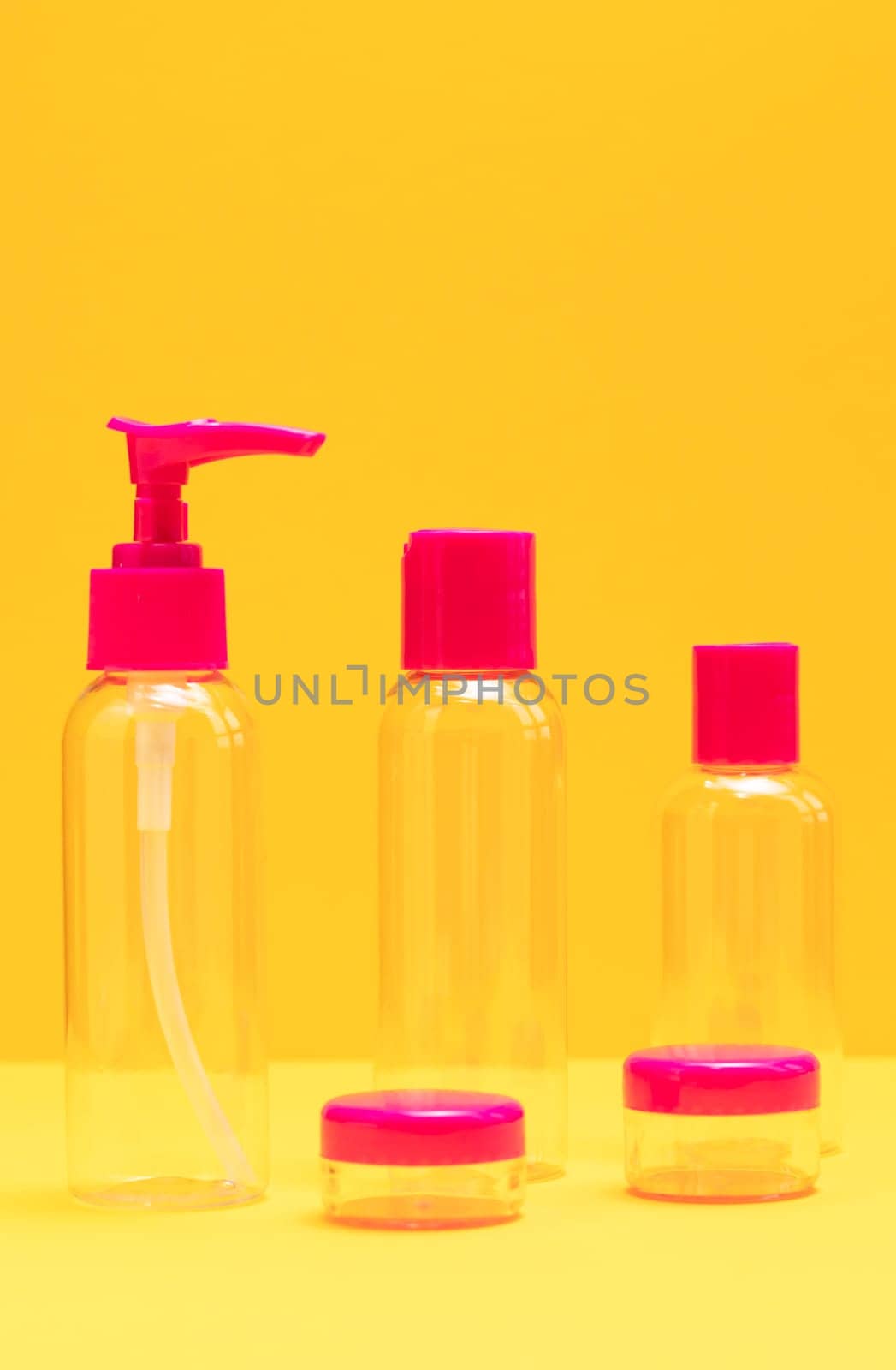 Closeup fuchsia travel bottle kit for liquids, cream. Toiletries Beauty Kit on yellow orange background. Airplane approved luggage reusable container size. Summer time, vacation concept. Vertical.