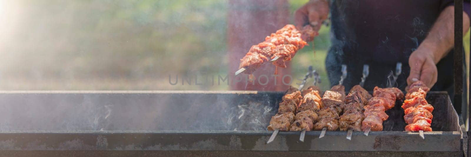 A man fries kebabs on skewers on a grill. Organization of a picnic in nature. by SERSOL