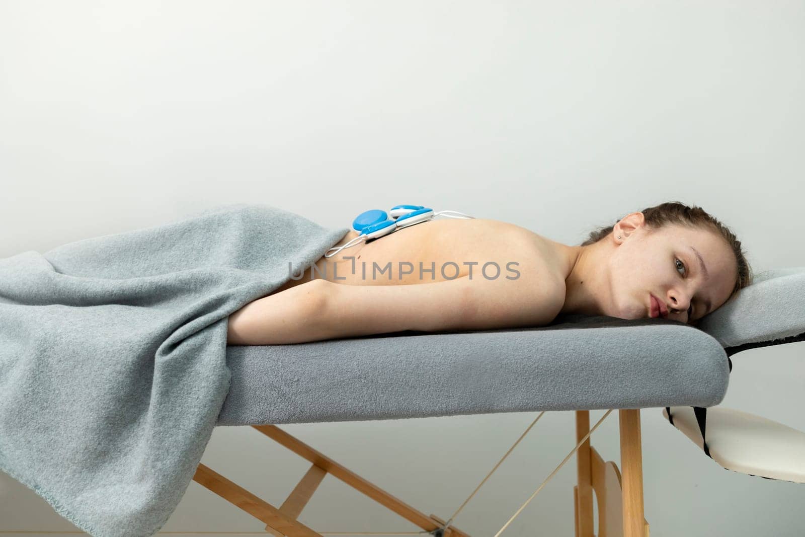 CCaucasian Girl With Cerebral Palsy, Scoliosis Lying on Couch, Getting Wireless Electric Muscle Stimulator Massage. Pain Treatment of Woman's Back. Rehabilitation, Medical Equipment. Horizontal plane by netatsi