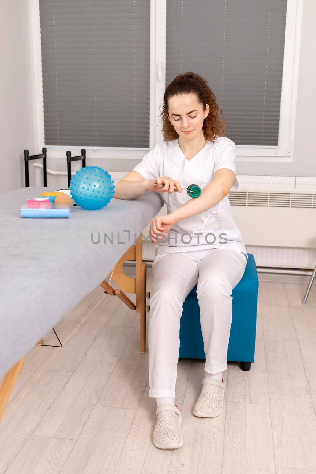 Rehabilitation Specialist, Physical Therapist With Rehab Tools, Foam Roller,Massage Ball With Pimples, Mesoroller With Titanium Needles, Kinesiology Tape On Couch in Therapeutic Room. Vertical plane