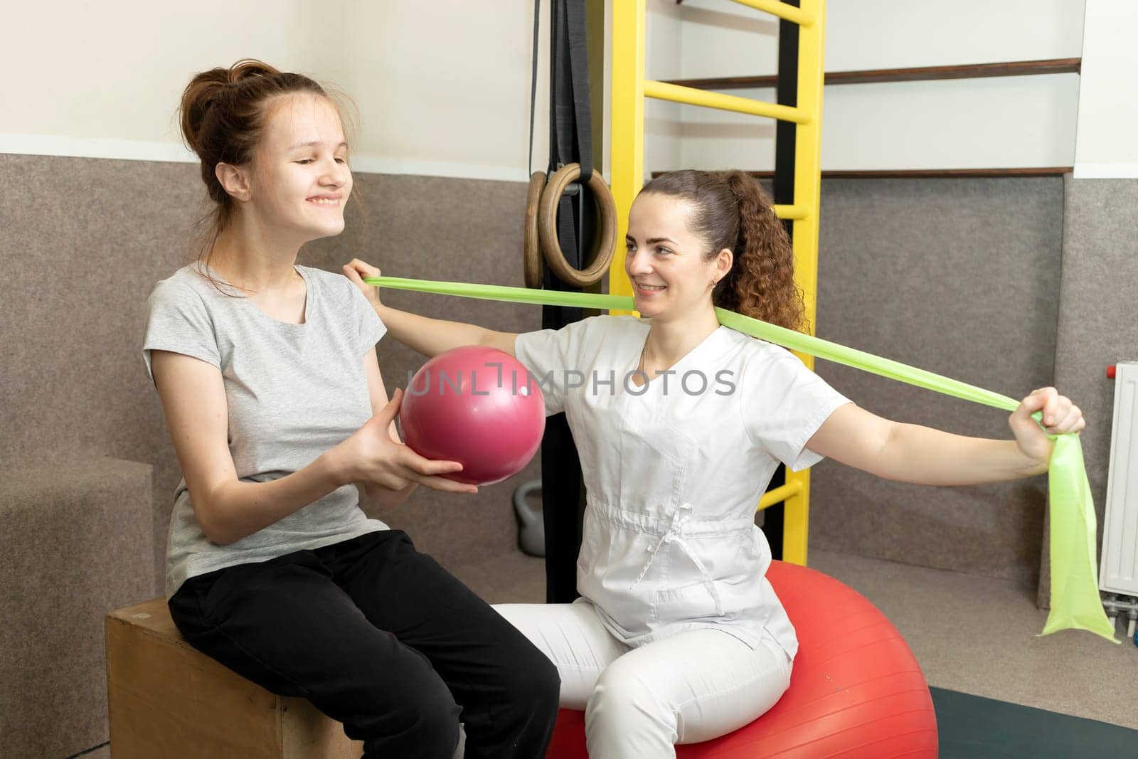 Smiling Child, Teenage Girl With Disability Does Physical Exercises With Support Of Rehabilitation Specialist, Physical Therapist. Rehabilitation. Musculoskeletal Disorder. Horizontal plane by netatsi