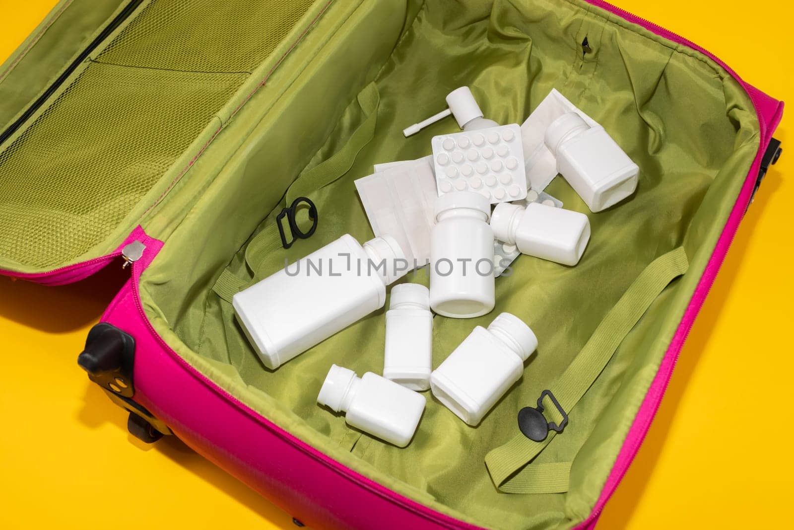 Travel Health Insurance Concept. Trip Pink Suitcase, Bag Full of Medication: Pills, Tablet Bottles, Containers, Adhesive plaster, Throat Oral Spray On Yellow Background. Closeup flat lay horizontal.