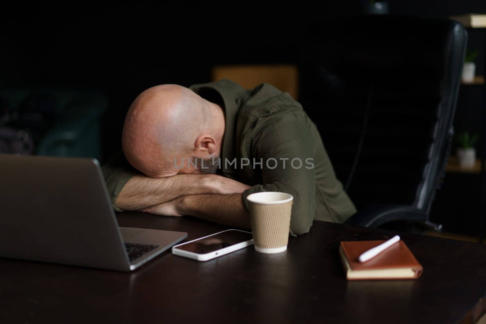 Tired mid-aged worker sleeping with head resting on table near laptop. Concept of age-related changes depicted, highlighting impact of exhaustion and fatigue on individuals as they navigate challenges of work. . High quality photo