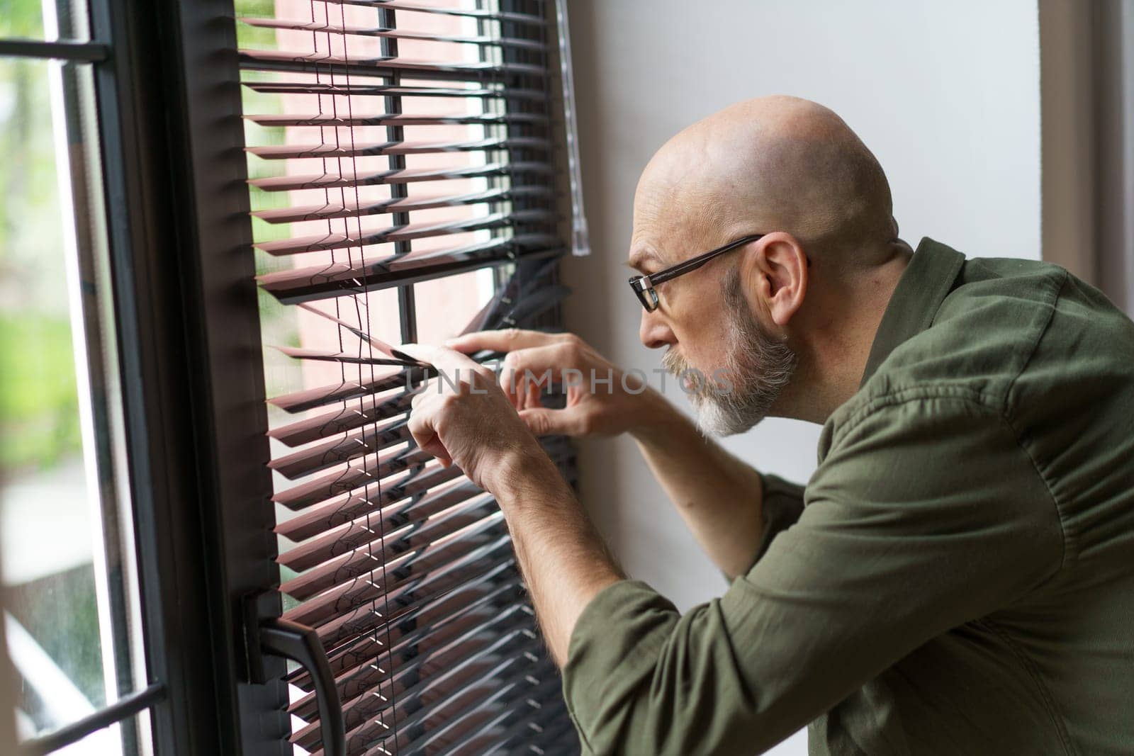 Concept of neighbors through perspective of old man standing near window and watching outside world. Senior's curiosity and engagement with the community around him. . High quality photo