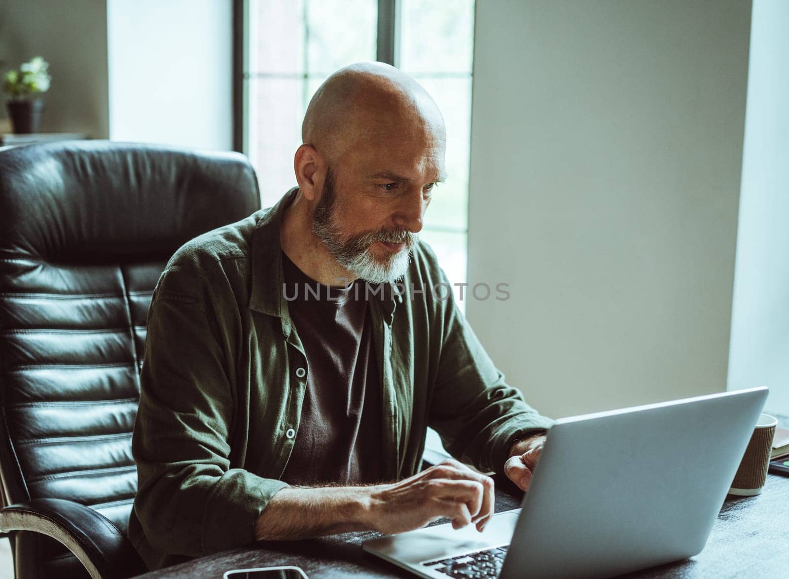 Man deeply concentrated on work as freelancer. With unwavering focus and passion, he immerses himself in his tasks within office space, situated across window. High quality photo
