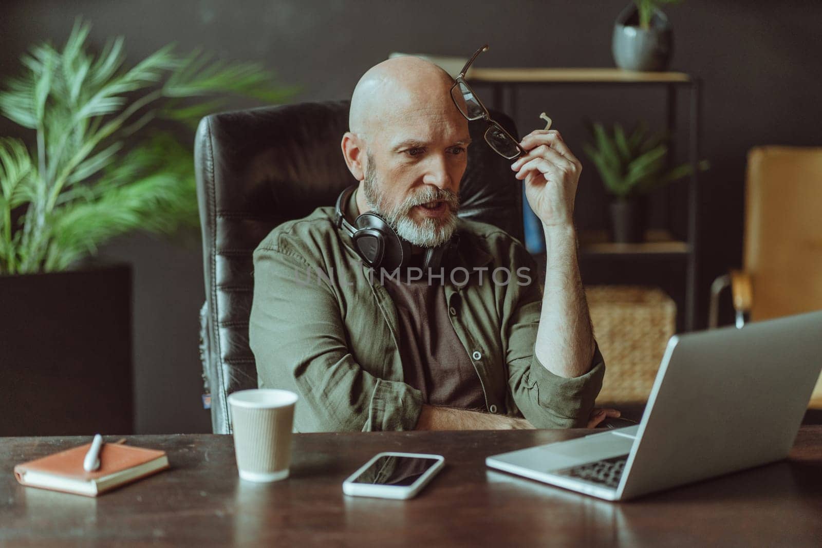 Shocked mature senior man captured reading news on laptop. Man, with distinguished silver beard, in closed pose as he looks intensely at computer screen while sitting at home. . High quality photo