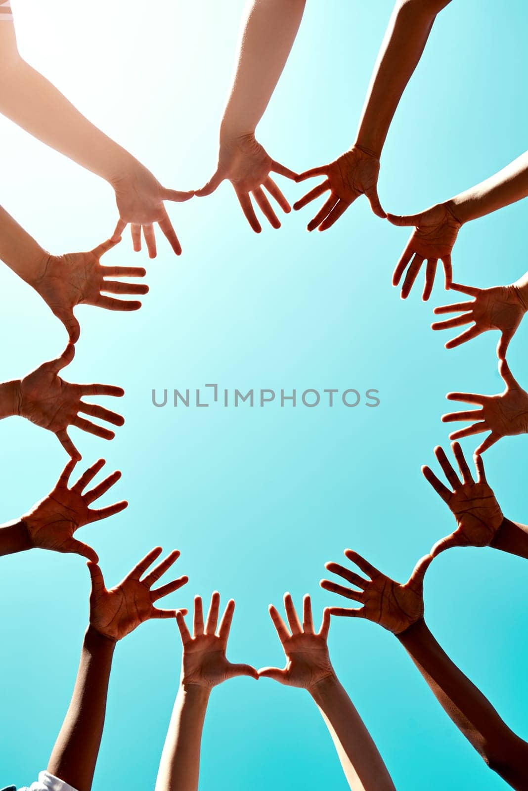 Community, support with hands in air and in blue sky outdoors for unity. Diversity or collaboration, sunlight and group of people with their hand in a circle for solidarity or trust with lens flare.