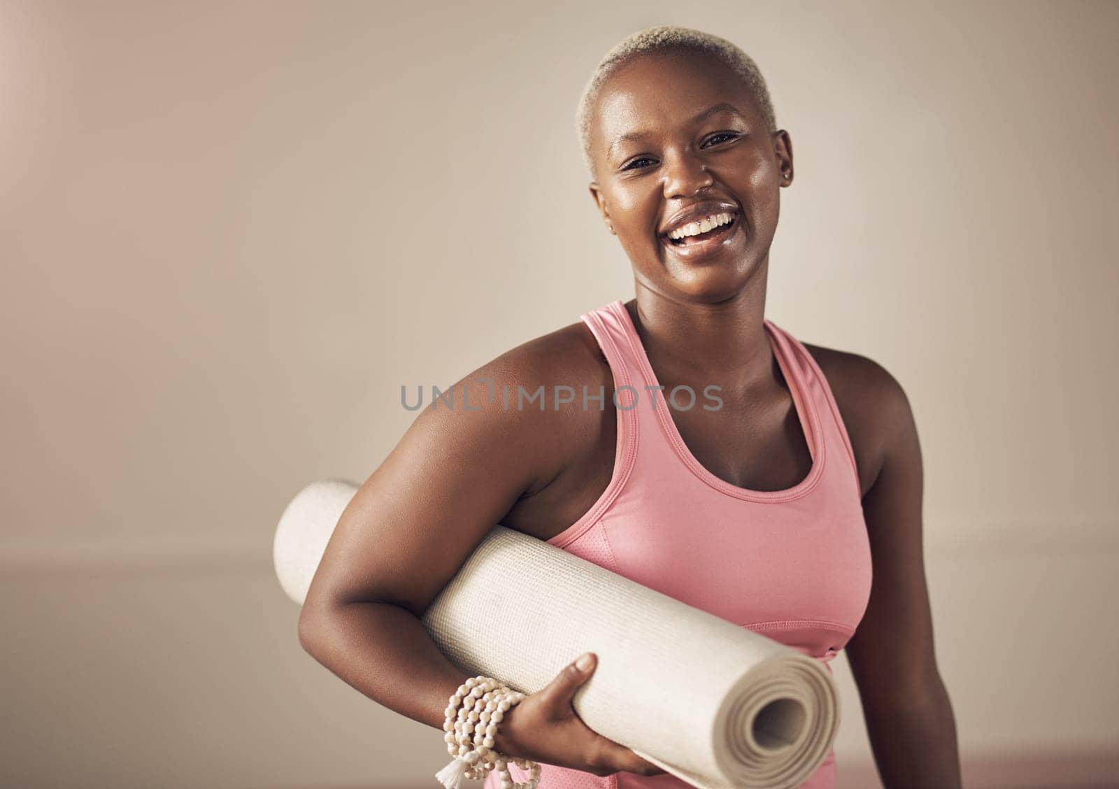 Smiling my way out the yoga studio. Cropped portrait of an attractive young woman standing alone and holding her yoga mat before an indoor yoga session. by YuriArcurs