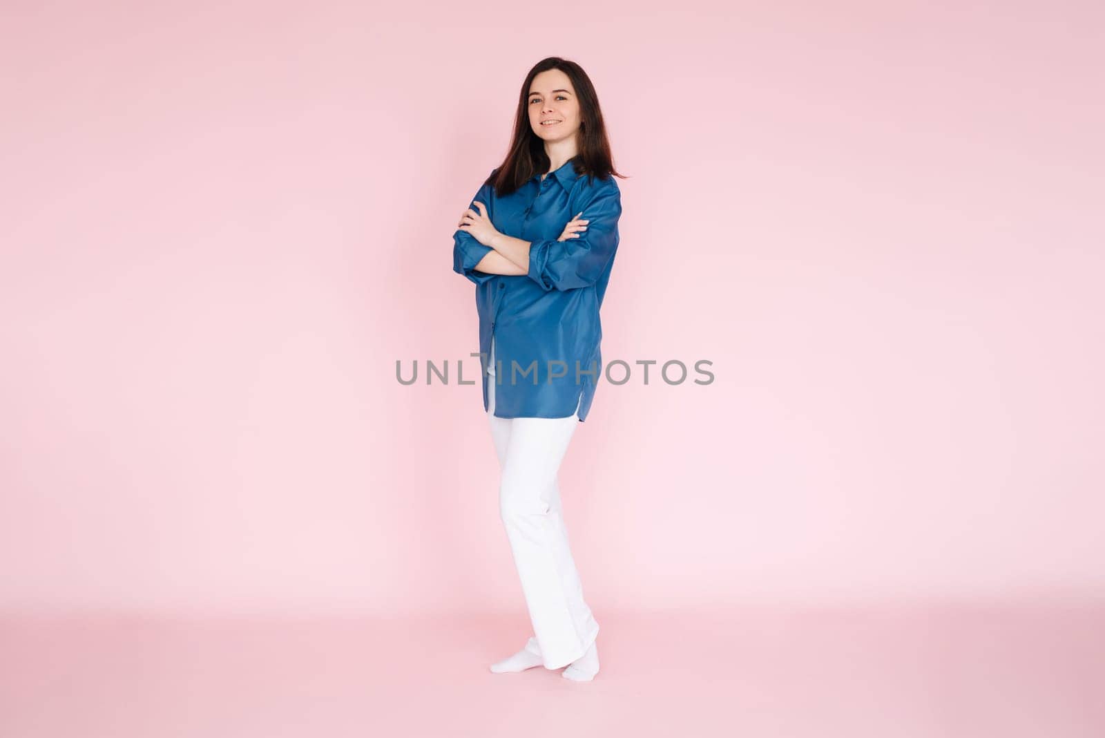 Portrait of professional businesswoman in smart casual attire standing confidently with folded hands, isolated on a pink background.