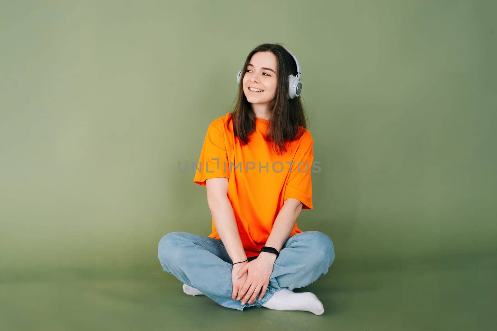Portrait of a dreamy woman with headphones looking into the distance, isolated on a vibrant green background.
