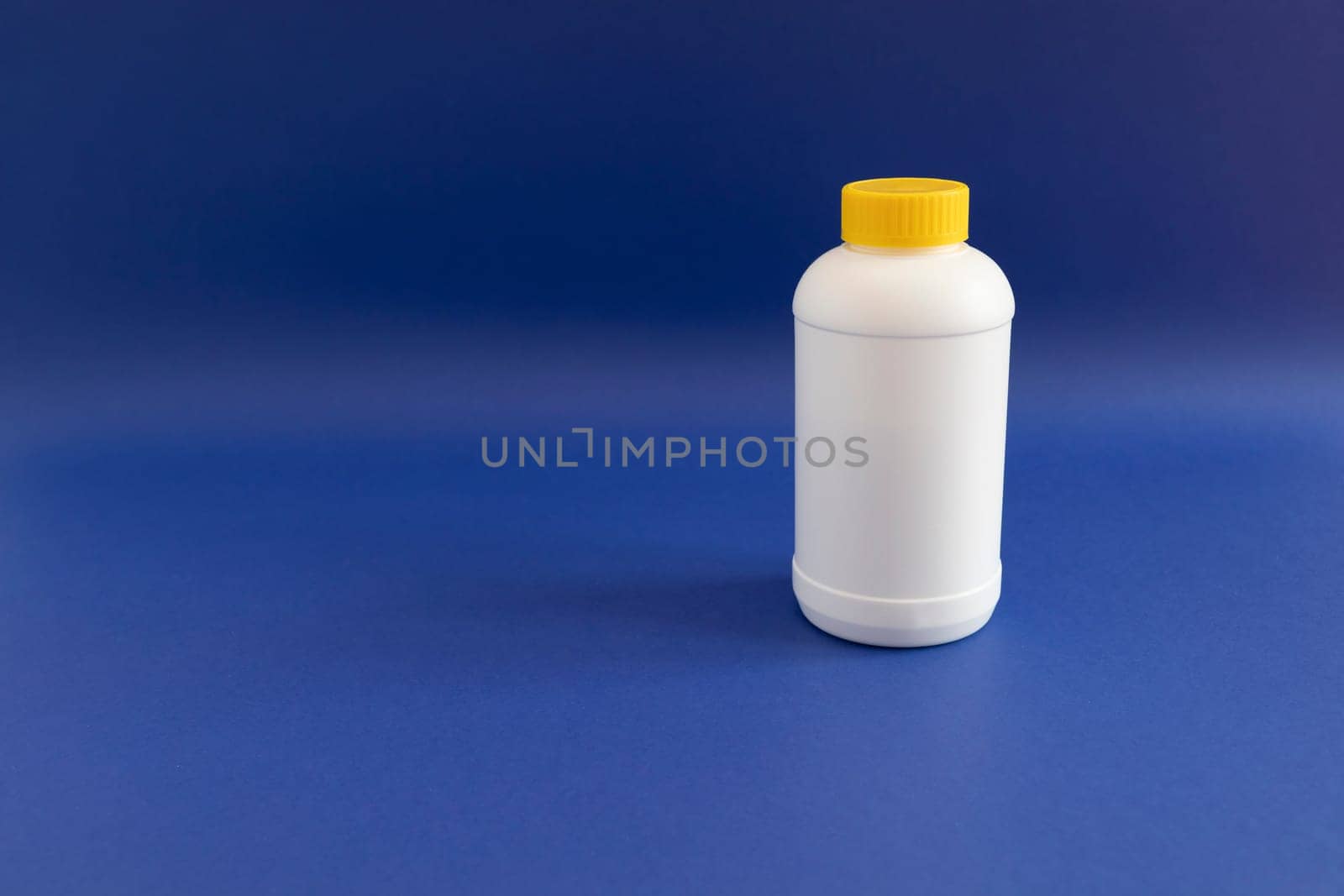 White Plastic Bottle, Yellow Cap With Pipe Granules Cleaner On Purple Blue Background. Removal Of Blockage In Sink, Shower With Special Chemicals. Cleaning Clog In Kitchen,Bathroom. Copyspace For Text