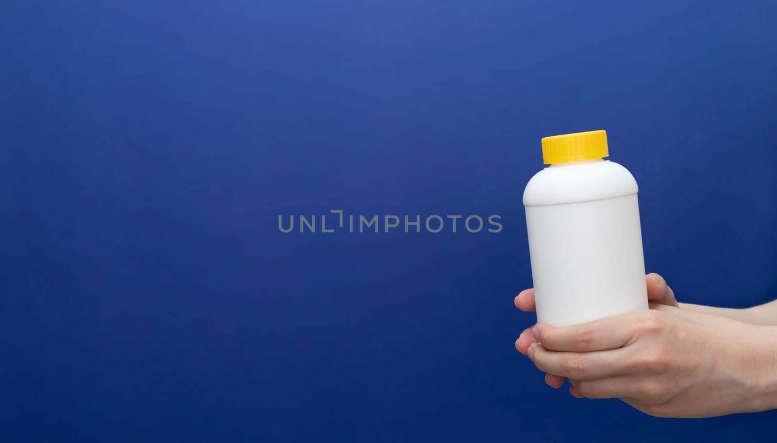 Banner Human Hand Holds White Bottle With Pipe Cleaner Granules. Removal Of Blockage In Sink, Shower With Special Chemicals. Cleaning Clog In Kitchen, Bathroom. Blue Background, Copy space For Text.