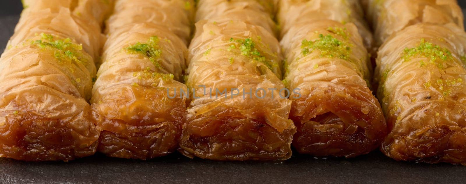 Pieces of baked baklava in honey and sprinkled with pistachios on a black board, close up