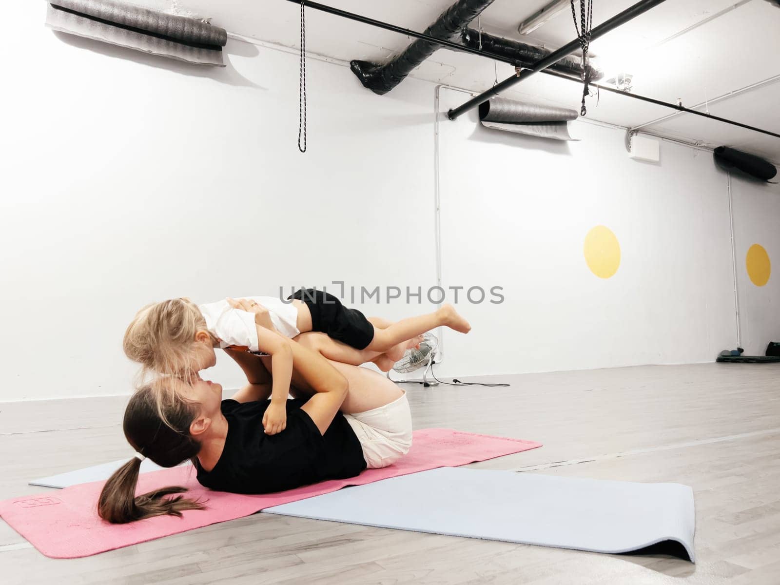 Mom holds a little girl on bent legs lying on a mat in the gym. High quality photo
