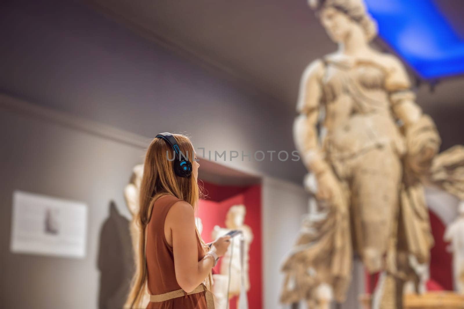 Portrait of contemporary young woman looking at sculptures and listening to audio guide at museum exhibition.
