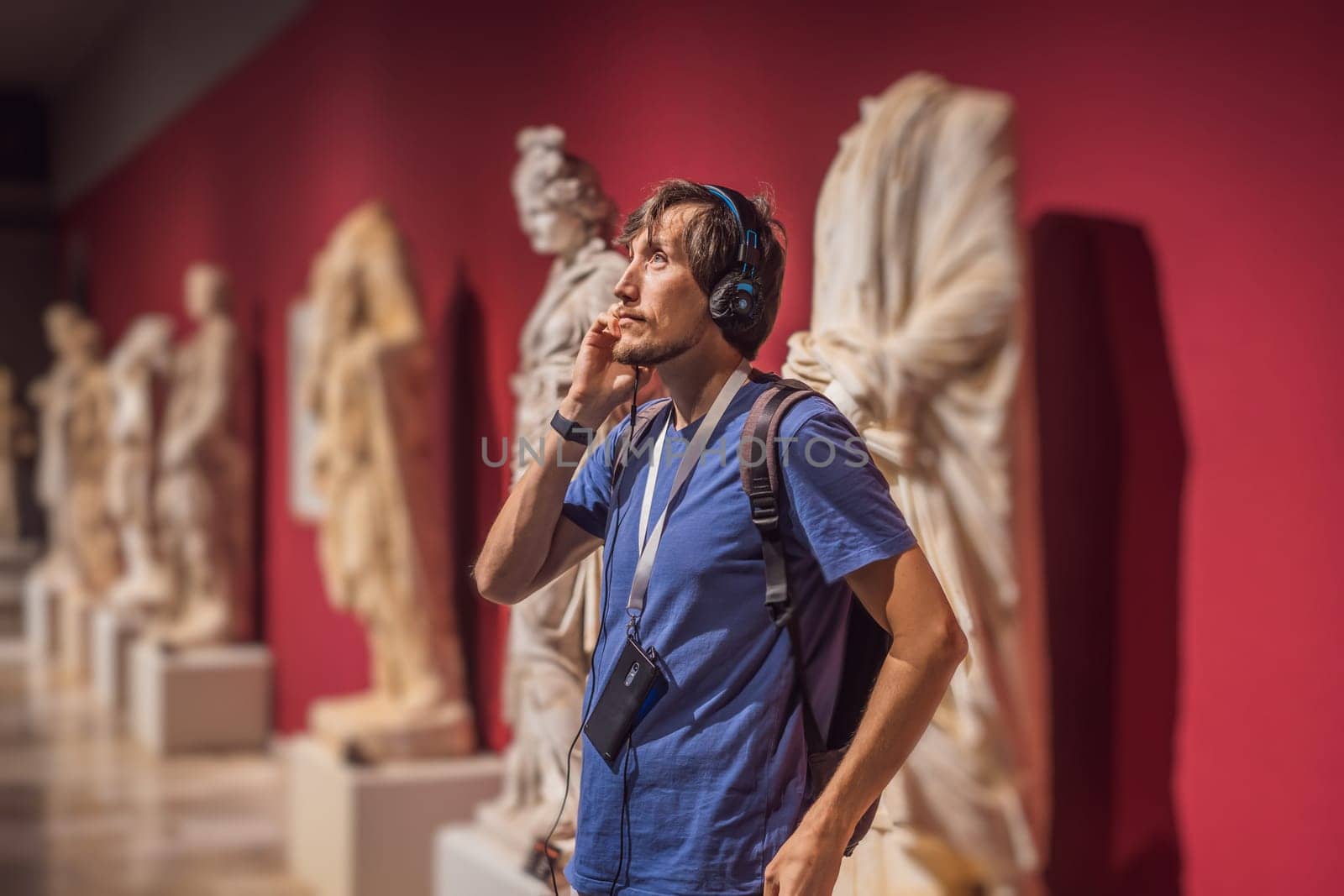 Portrait of contemporary man looking at sculptures and listening to audio guide at museum exhibition.
