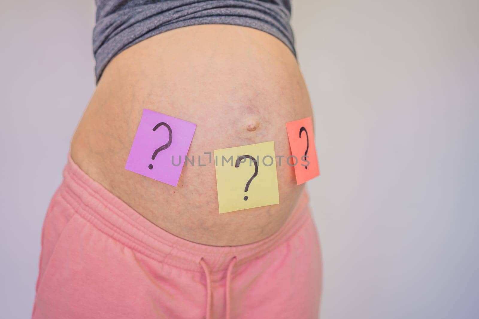 Choosing baby name. Confused pregnant woman with question marks on paper stickers on tummy.
