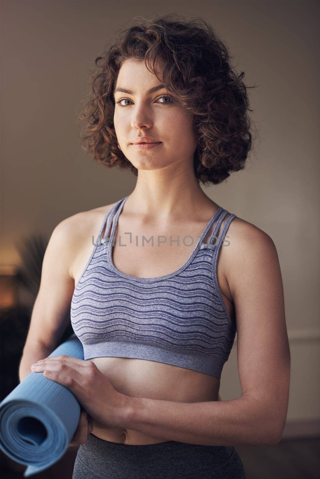 A day without yoga is a day wasted. Cropped portrait of an attractive young woman standing alone and holding her yoga mat before an indoor yoga session. by YuriArcurs