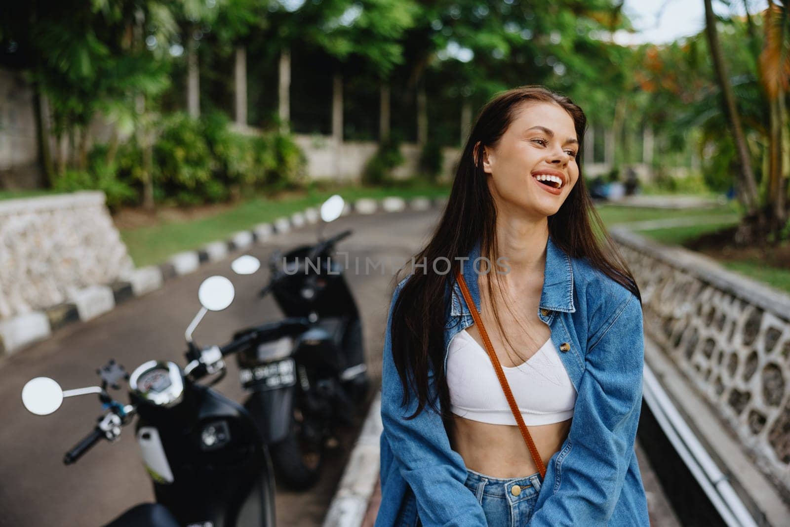 Portrait of a woman brunette smile with teeth walking outside against a backdrop of palm trees in the tropics, summer vacations and outdoor recreation, the carefree lifestyle of a freelance student. by SHOTPRIME