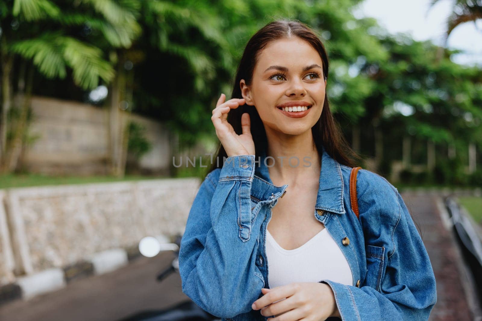 Portrait of a woman brunette smile with teeth walking outside against a backdrop of palm trees in the tropics, summer vacations and outdoor recreation, the carefree lifestyle of a freelance student. High quality photo