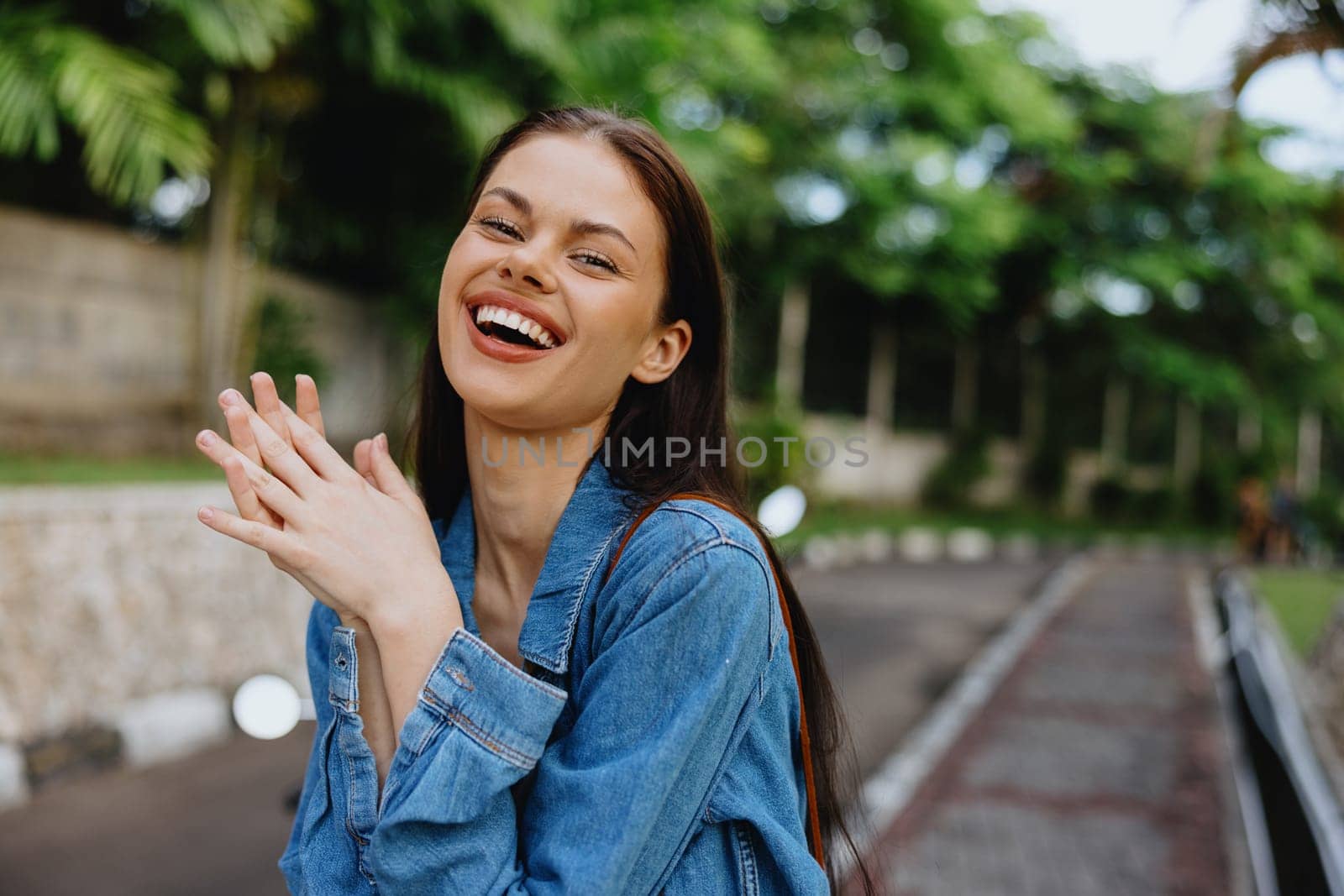 Portrait of a woman brunette smile with teeth walking outside against a backdrop of palm trees in the tropics, summer vacations and outdoor recreation, the carefree lifestyle of a freelance student. by SHOTPRIME