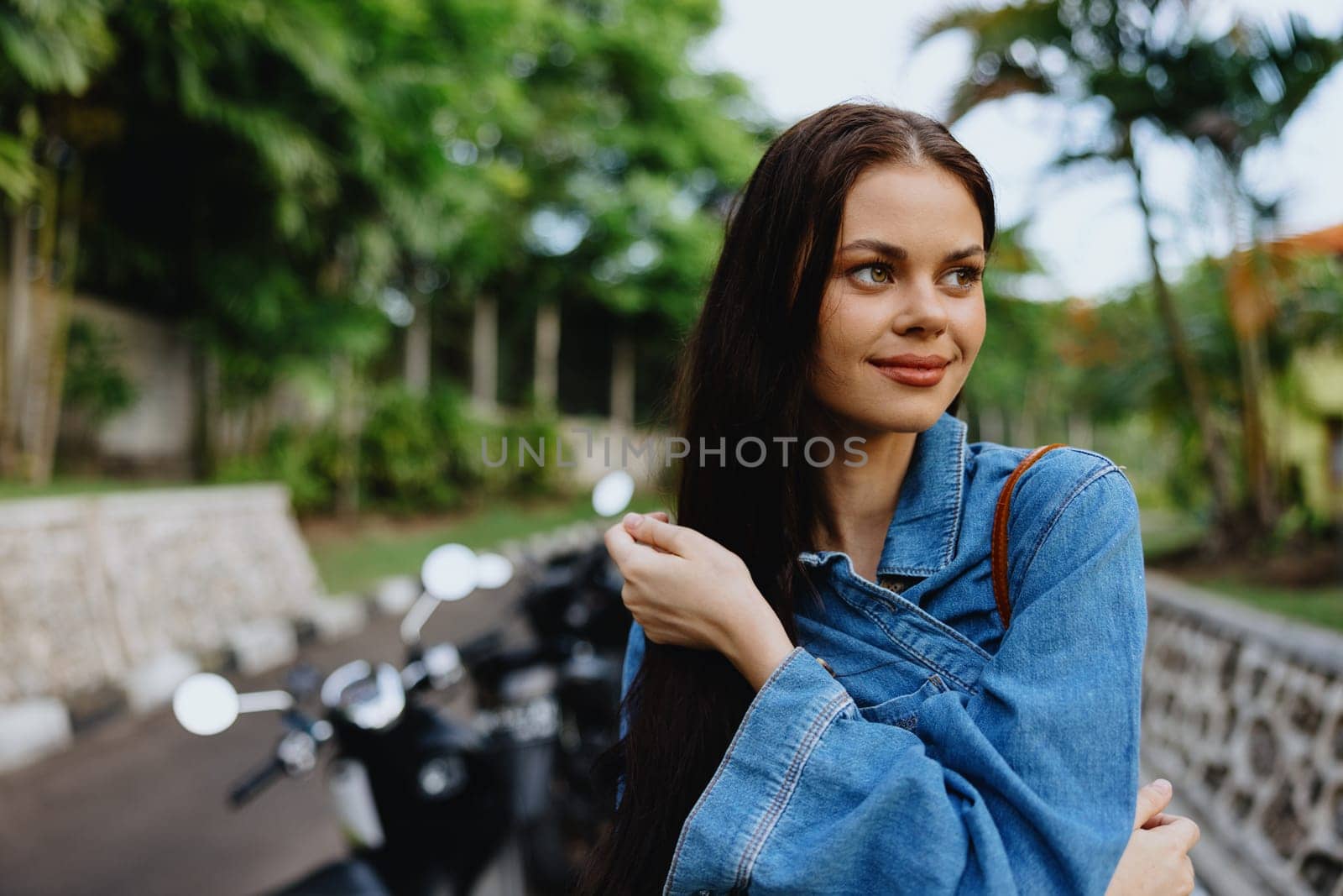 Portrait of a woman brunette smile with teeth walking outside against a backdrop of palm trees in the tropics, summer vacations and outdoor recreation, the carefree lifestyle of a freelance student. by SHOTPRIME