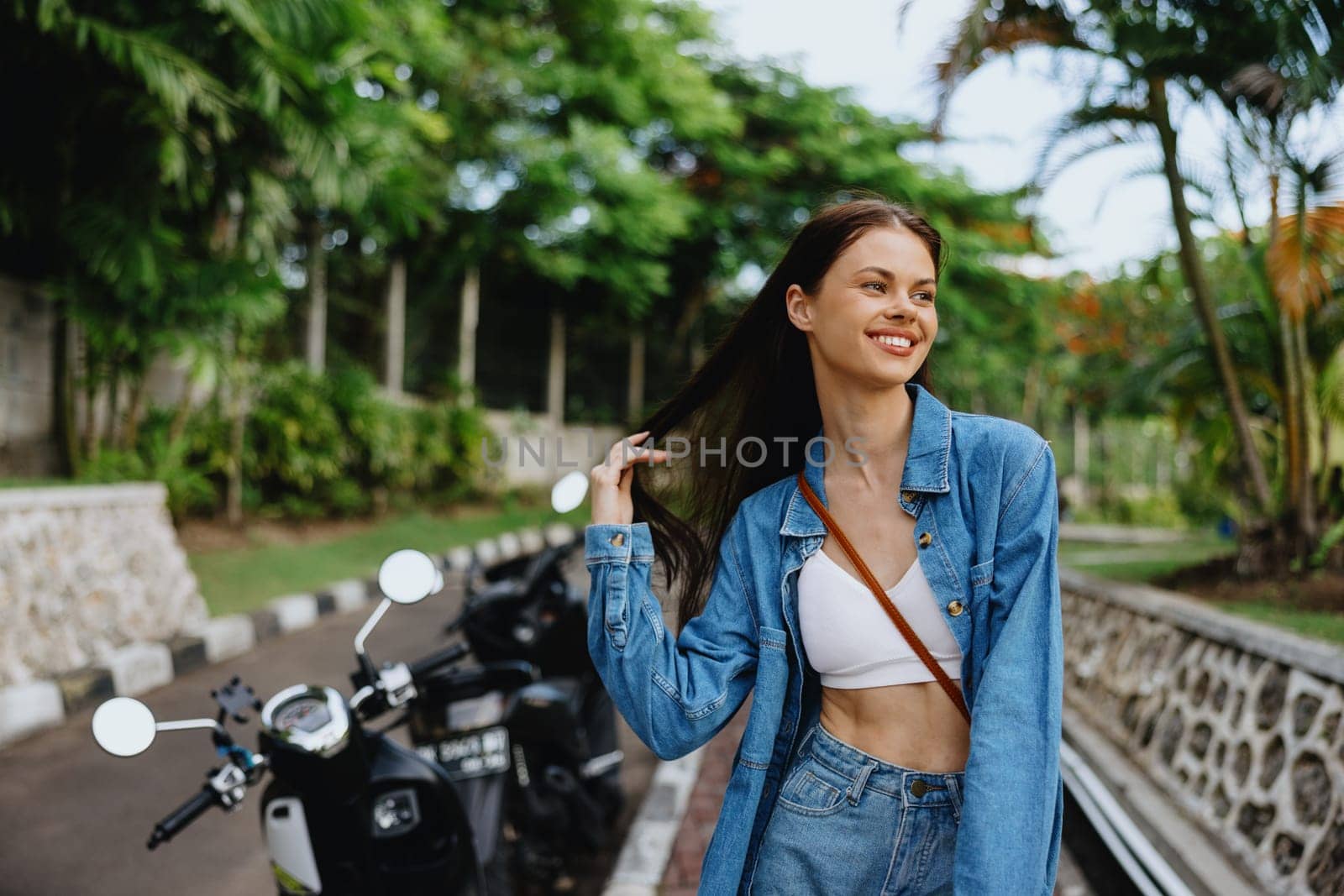 Portrait of a woman brunette smile with teeth walking outside against a backdrop of palm trees in the tropics, summer vacations and outdoor recreation, the carefree lifestyle of a freelance student. by SHOTPRIME