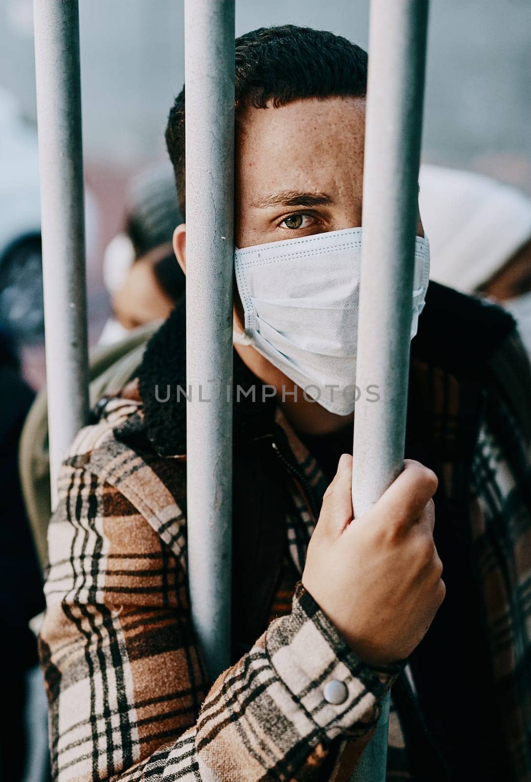 Sick, refugee of a young covid patient in quarantine to cross the border with a medical face mask. Foreign man in a prison crowd during a pandemic following healthcare safety rules of the virus. by YuriArcurs