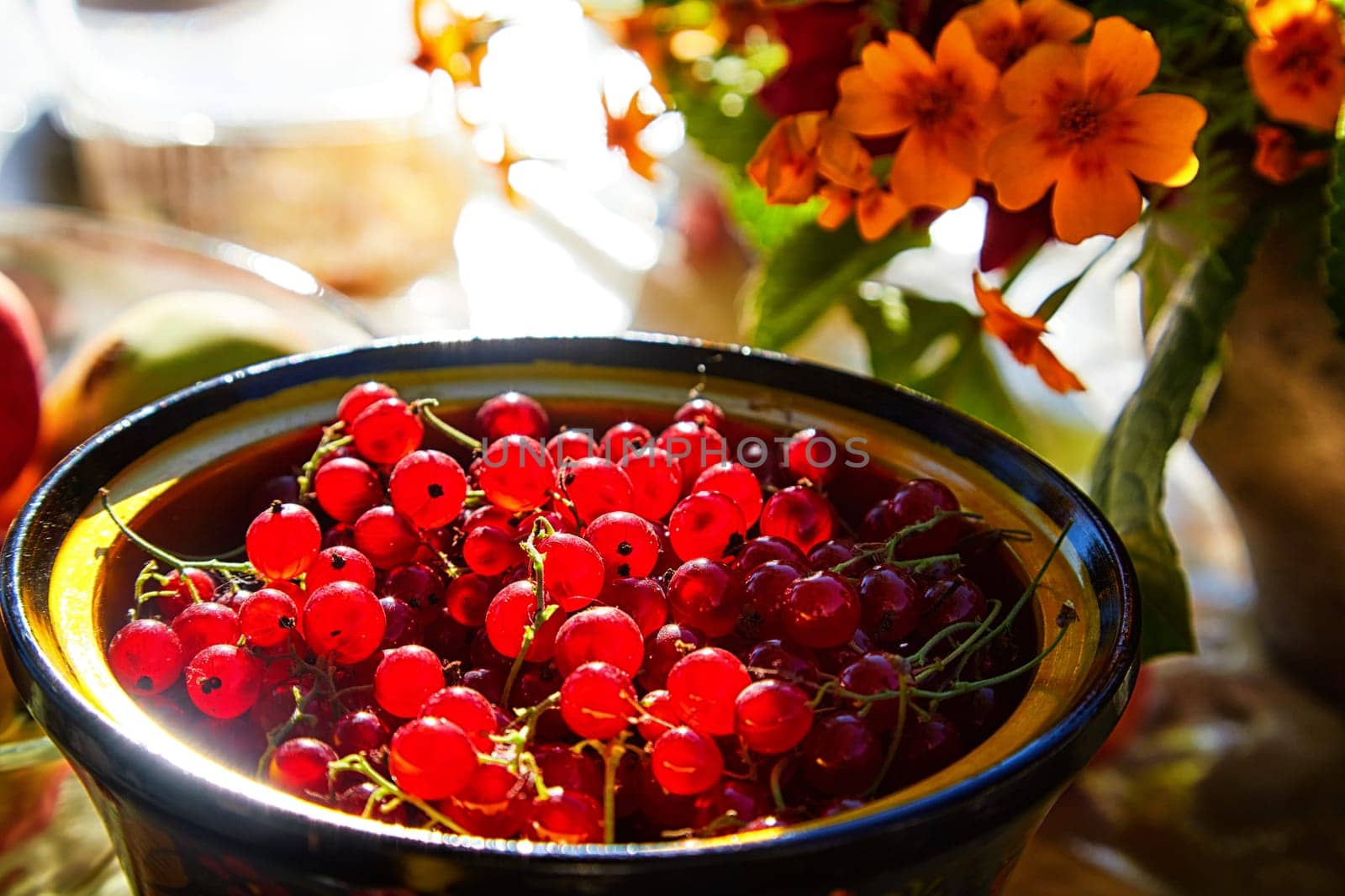 Red currant berries in a wooden plate on the table and a blurred background with red flowers