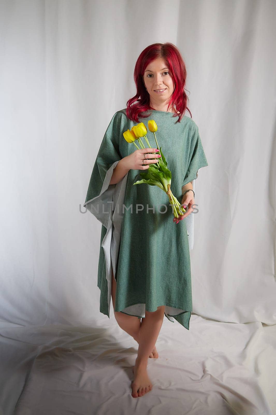 Beautiful woman with red hair in yellow dress on light background holds tulips. Inernational woman's day 8 March