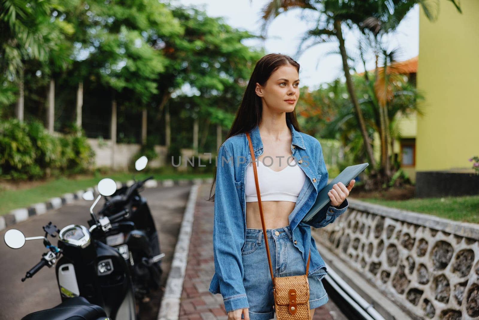 Woman smiling walking in the park outside with laptop freelancer against a backdrop of green palm trees in summer, tropical backdrop, blogger on a trip, work online. High quality photo