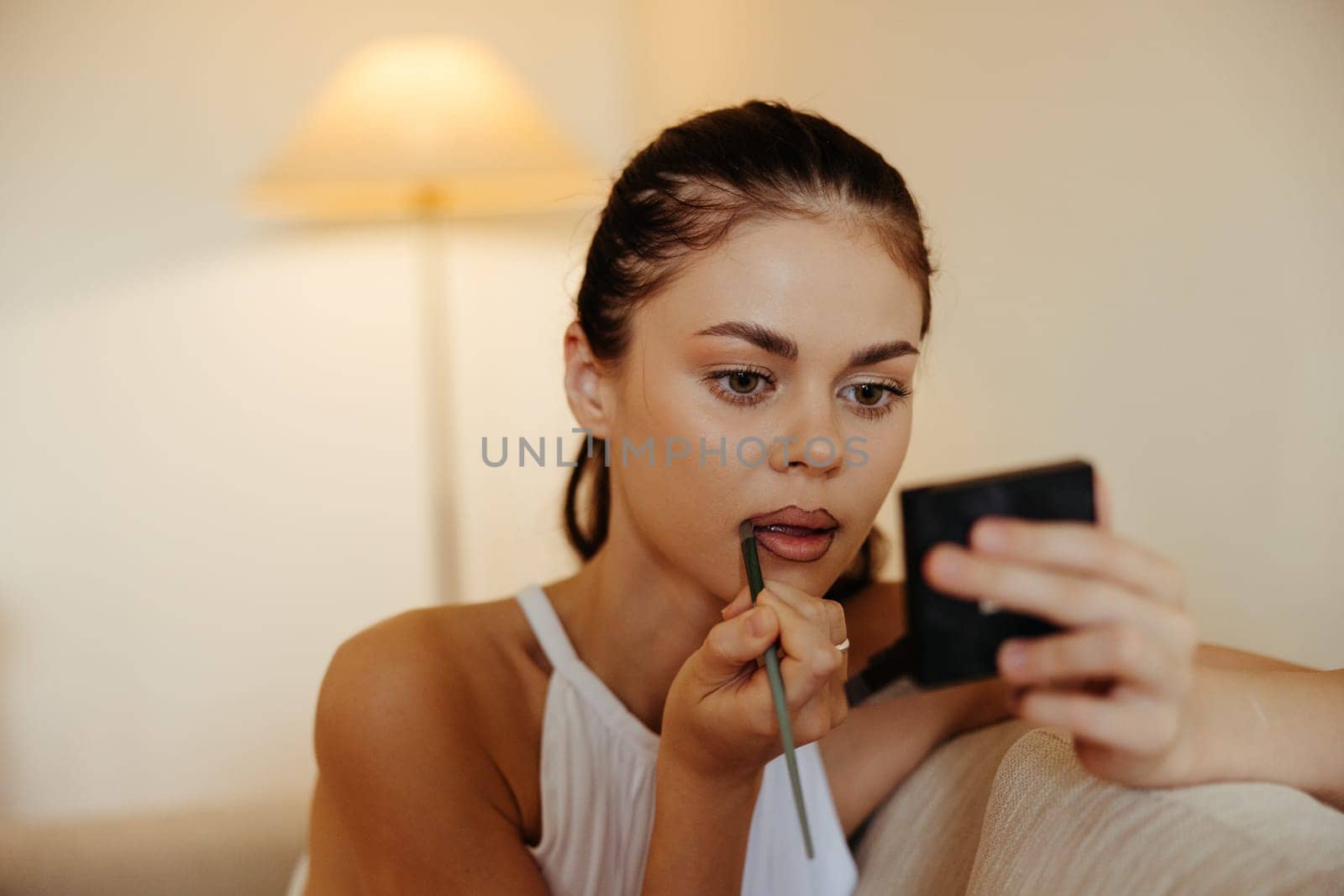 A woman at home looks in the mirror and applies makeup lipstick, beauty concept, problem skin care with acne, home makeup. High quality photo