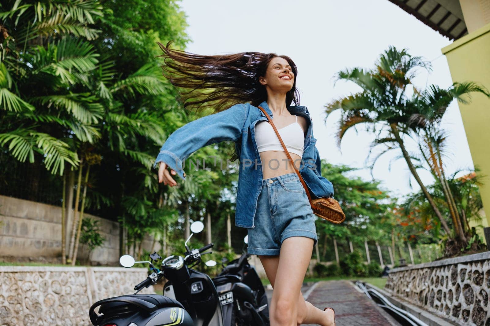 Portrait woman brunette smile with teeth running down the street against backdrop of palm trees in the tropics, summer vacations and outdoor recreation, the carefree lifestyle of a freelance student. by SHOTPRIME