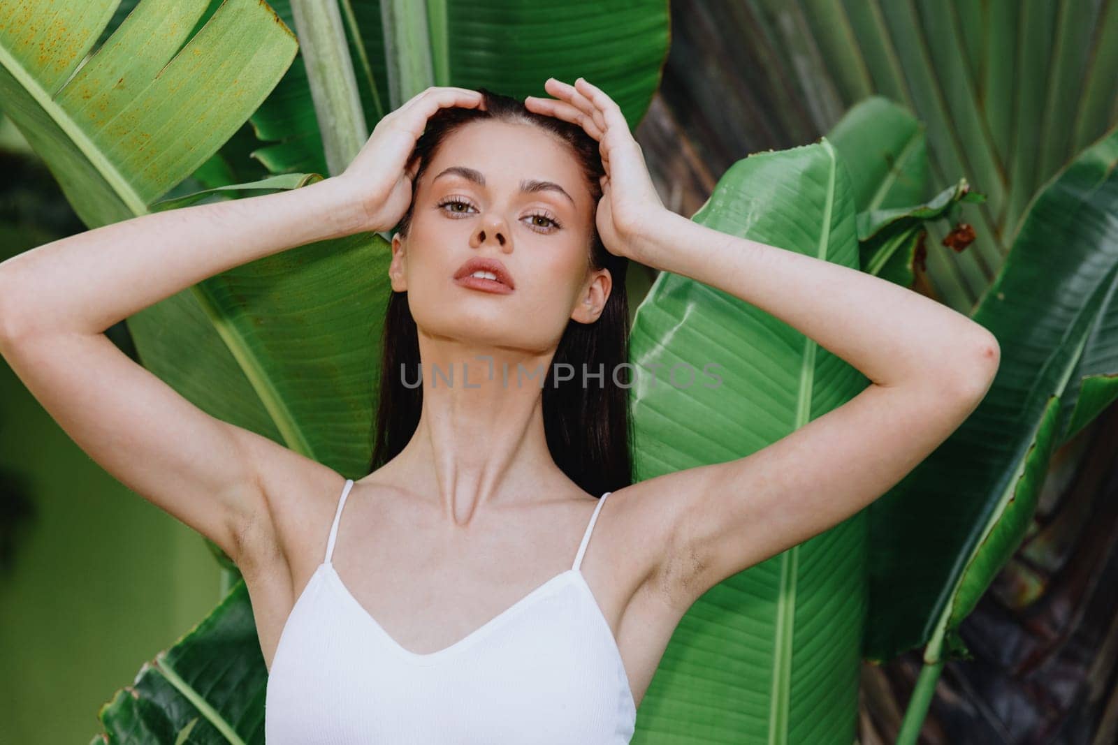 Beauty portrait of a young woman brunette with long hair in front of palm trees, face and body skin care concept, the tropics, advertising beauty products. High quality photo