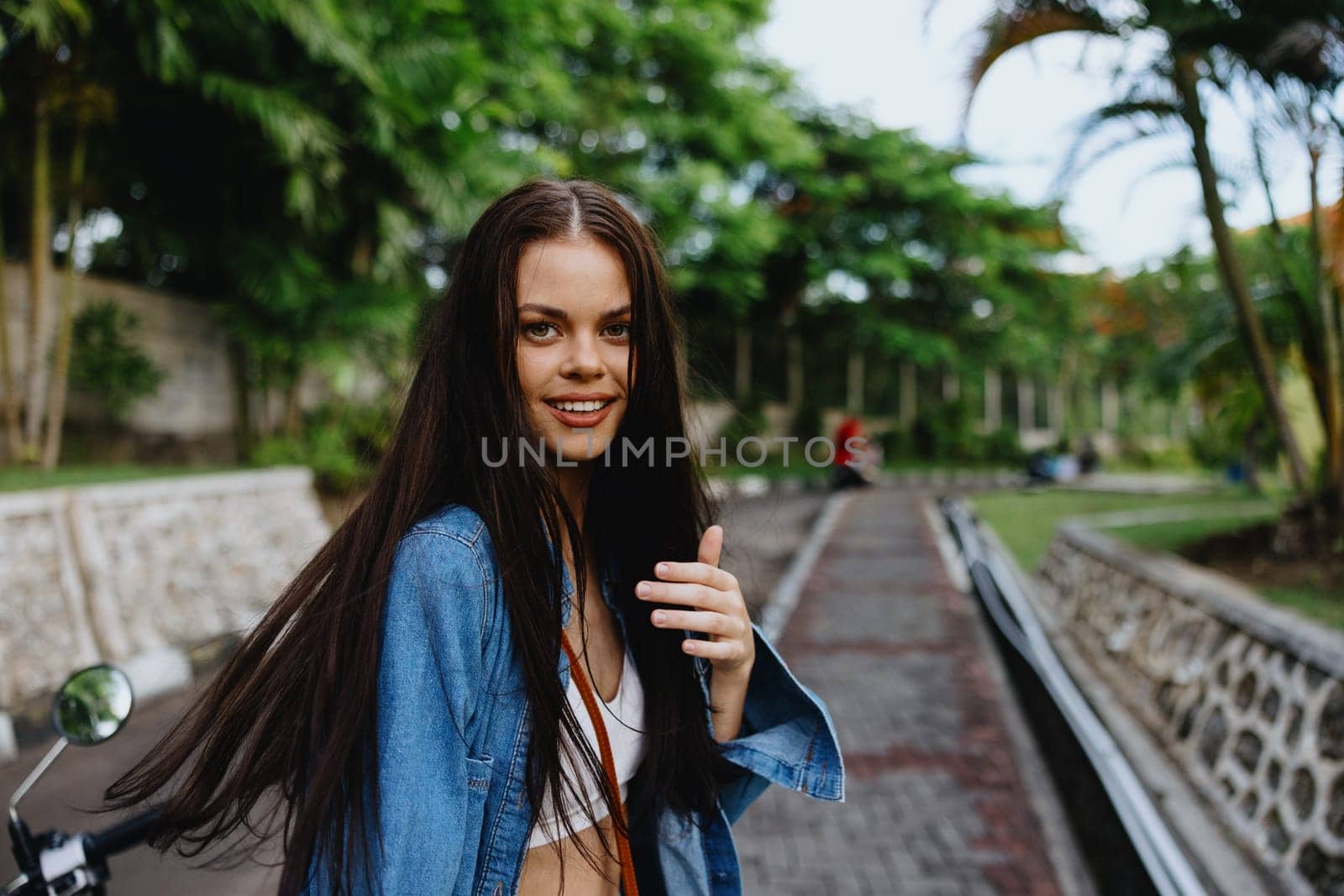 Portrait of woman brunette smile with teeth running down the street against backdrop palm trees in the tropics, summer vacations and outdoor recreation, the carefree lifestyle of a freelance student. by SHOTPRIME