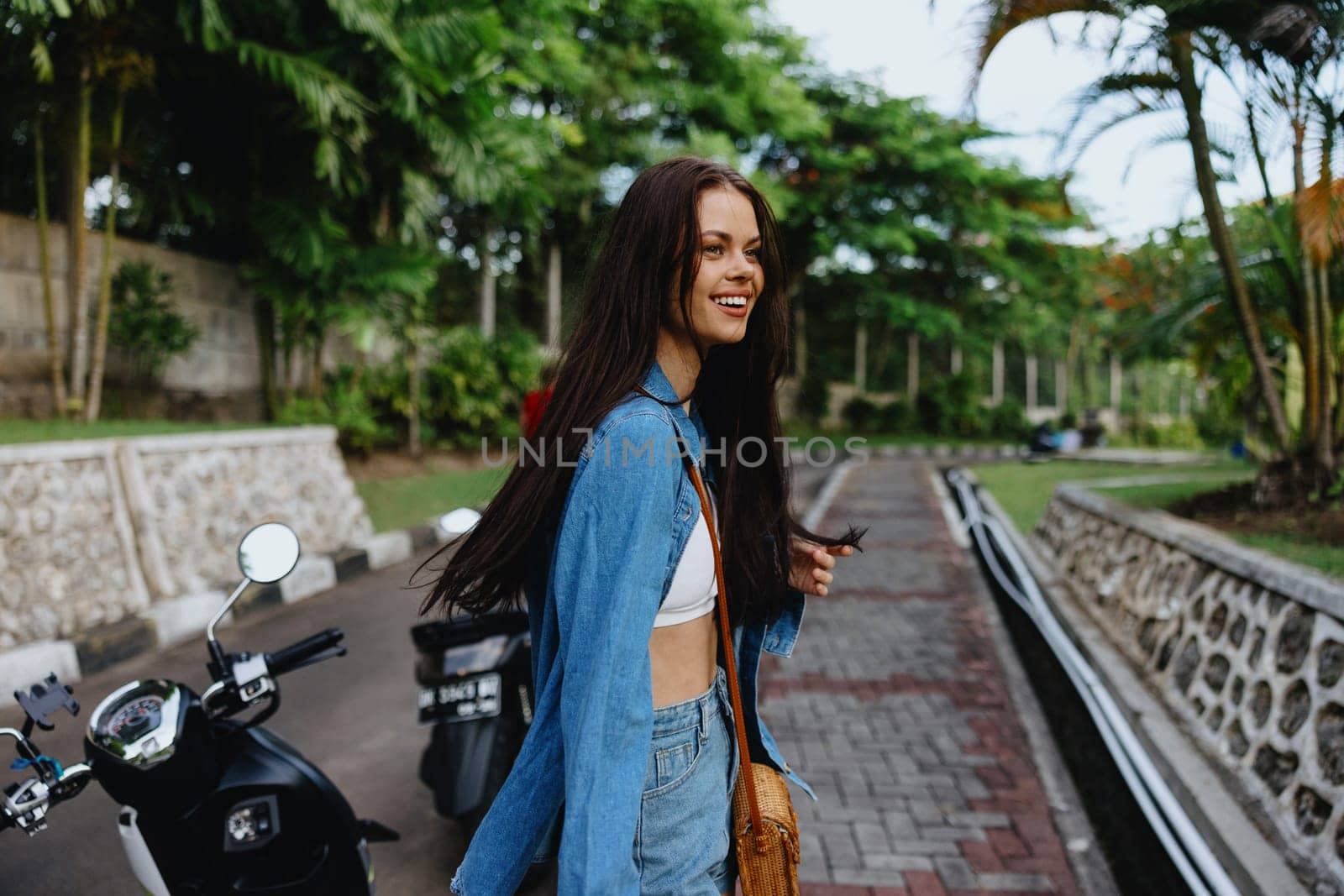 Portrait of woman brunette smile with teeth running down the street against backdrop palm trees in the tropics, summer vacations and outdoor recreation, the carefree lifestyle of a freelance student. by SHOTPRIME