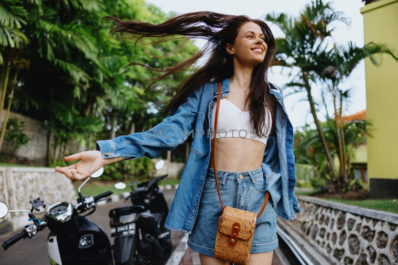 Portrait woman brunette smile with teeth running down the street against backdrop of palm trees in the tropics, summer vacations and outdoor recreation, the carefree lifestyle of a freelance student. by SHOTPRIME