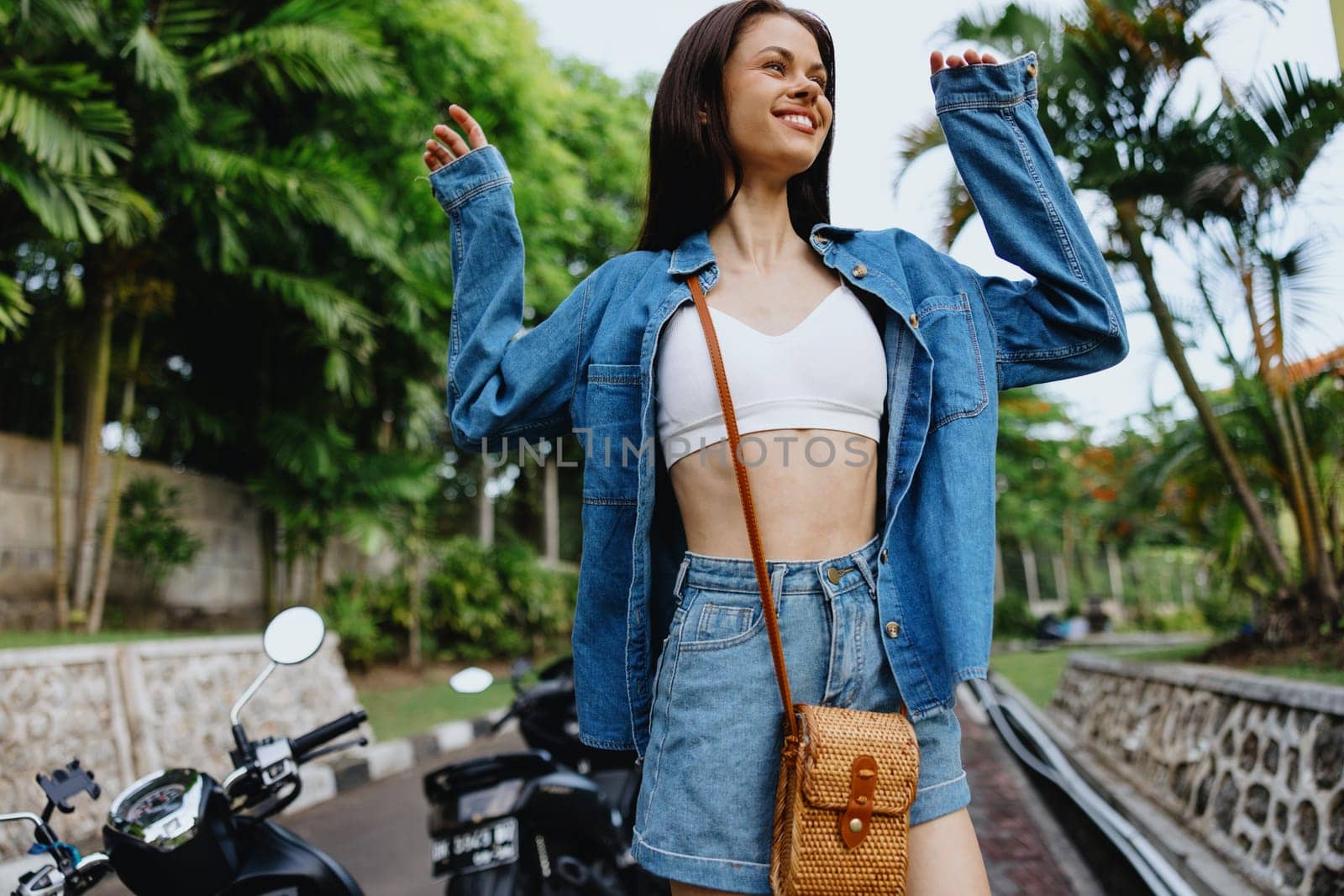 Portrait of a woman brunette smile with teeth walking outside against a backdrop of palm trees in the tropics, summer vacations and outdoor recreation, the carefree lifestyle of a freelance student. by SHOTPRIME