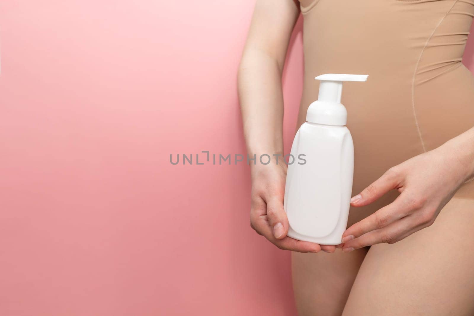 Woman Holds White Dispenser Bottle Of Hygiene Product, Washing, Cleansing Intimate Gel, Foam. Female Wears Beige Body On Pink Background. Mockup Branding Container, Horizontal, Copy space for text