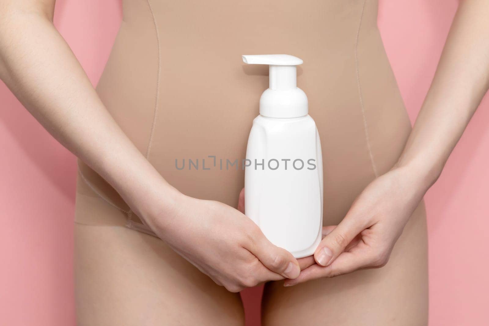Woman Holds White Bottle Of Hygiene Product, Washing, Cleansing Intimate Gel, Foam. Female Wears Beige Body On Pink Background. Mockup Branding Dispenser, Daily Body Care. Horizontal Plane, Closeup