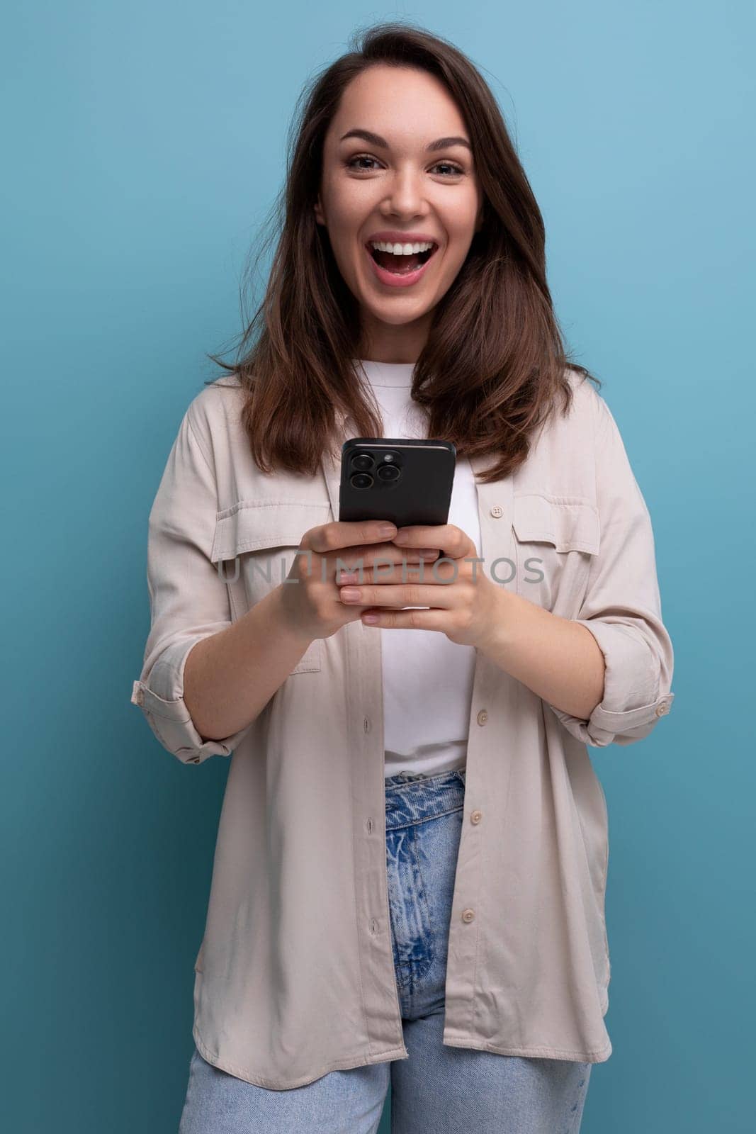 pretty brunette young brunette lady dressed in shirt and jeans chatting in smartphone by TRMK